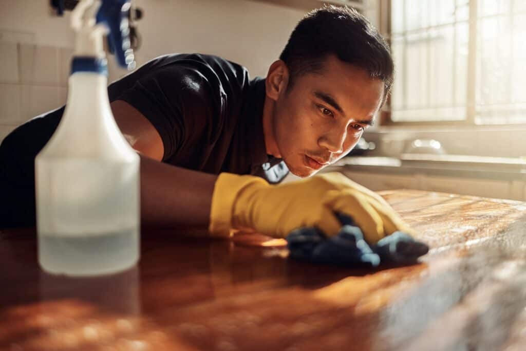 Shot of a young man disinfecting a kitchen counter at home