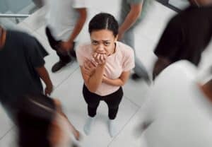 Shot of a young woman experiencing mental illness while being surrounded by people inside